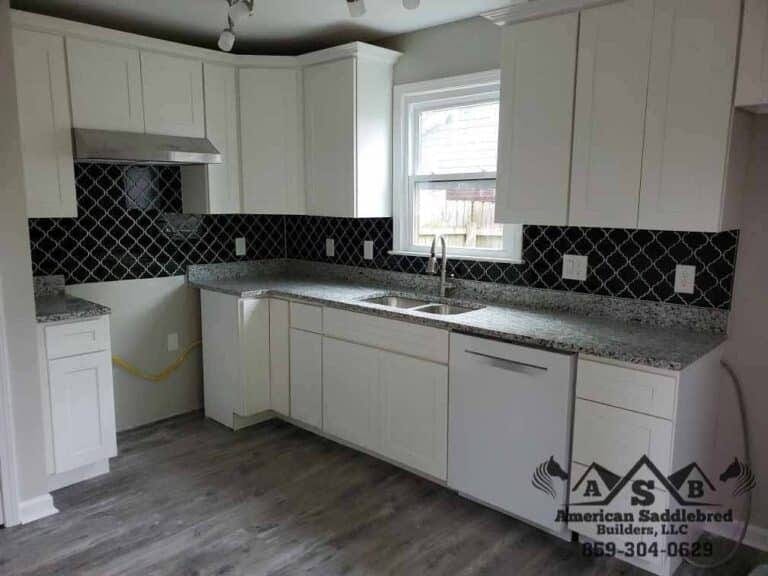 Contemporary white kitchen featuring gray granite counters and dark geometric backsplash design